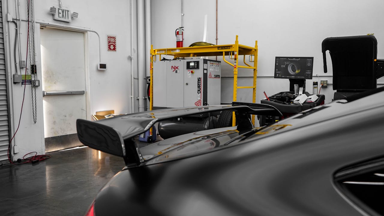 A sleek black sports car with a spoiler parked in a well-equipped garage.